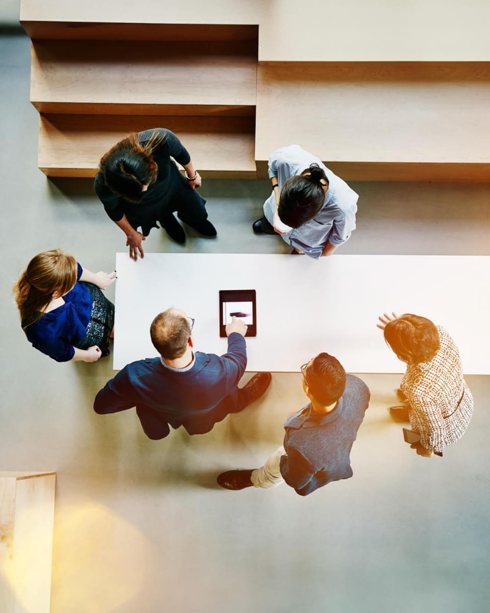 Top view of people standing around a table looking at a tablet.