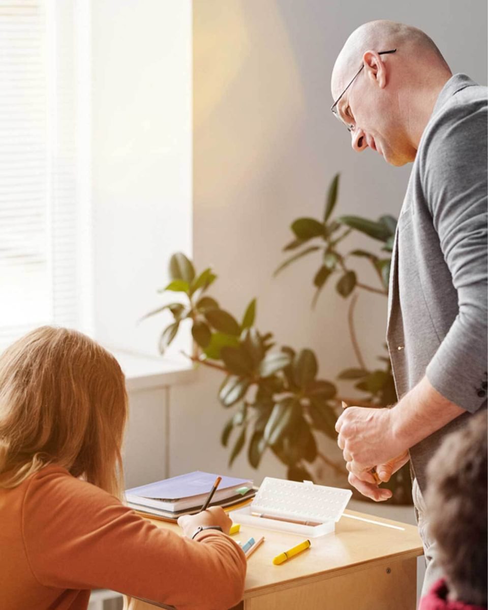 A teacher talking to student sitting at a desk.